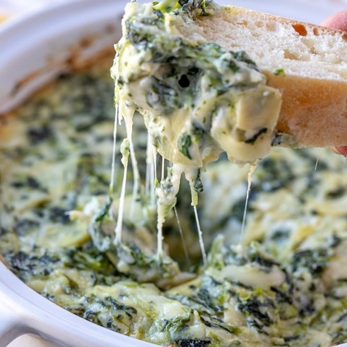 scooping cheesy spinach artichoke dip with baguette slices