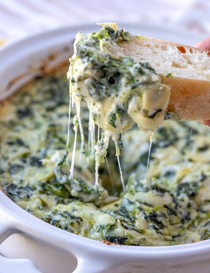 scooping cheesy spinach artichoke dip with baguette slices