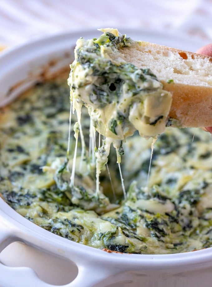 scooping cheesy spinach artichoke dip with baguette slices