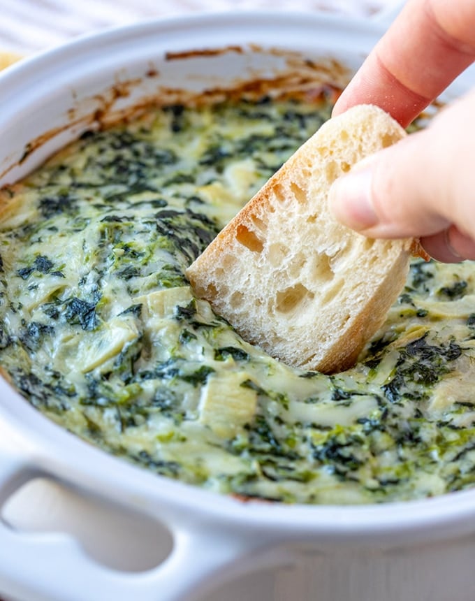 dipping sliced sourdough bread in spinach artichoke dip