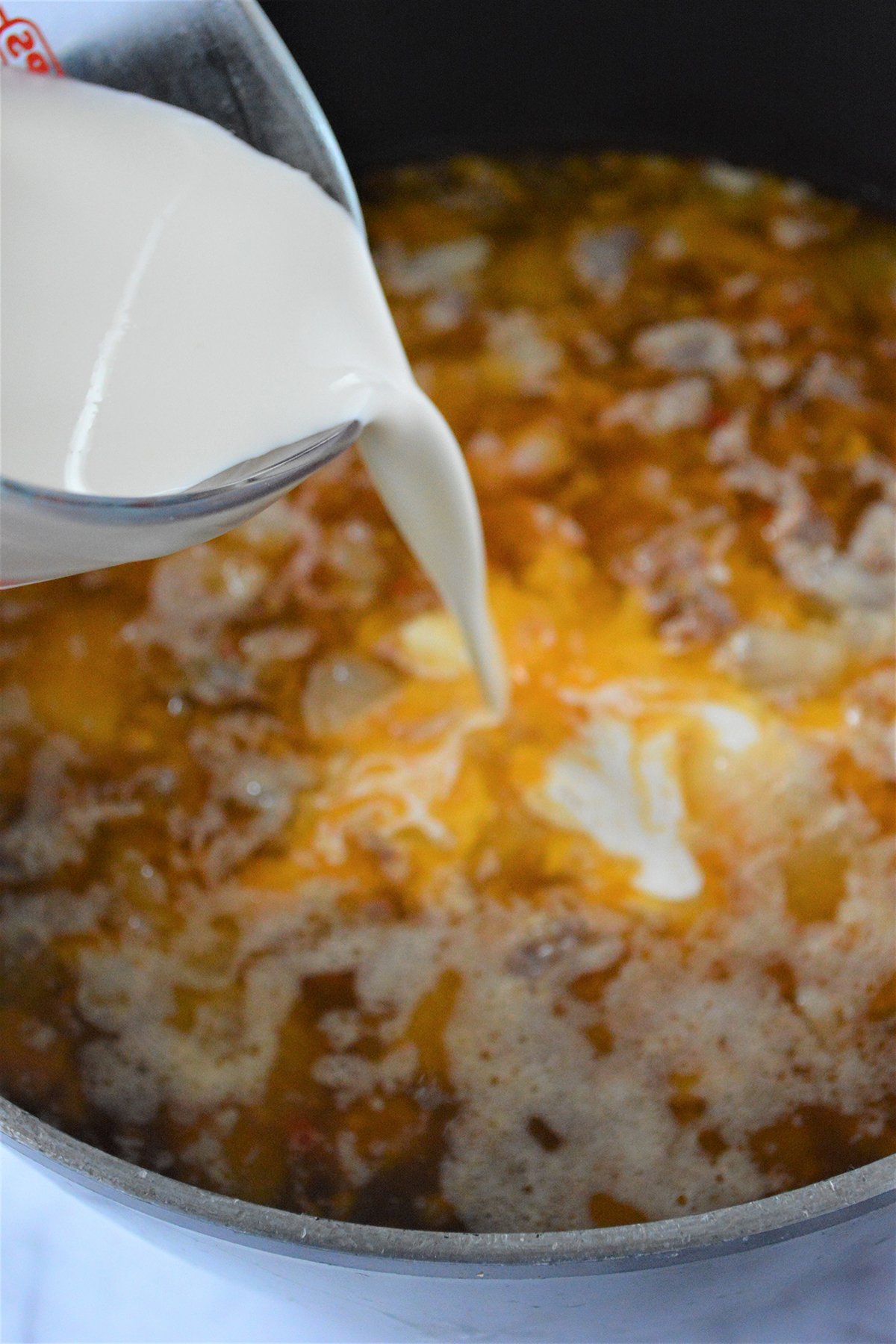 pouring heavy cream into a pot of Tuscan soup