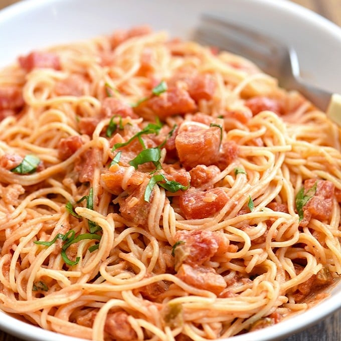 angel hair pasta tossed with chunky tomato cream sauce on white plate