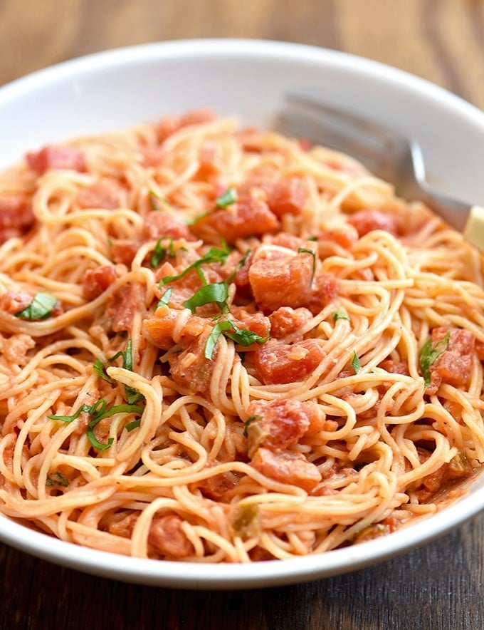 angel hair pasta tossed with chunky tomato cream sauce on white plate