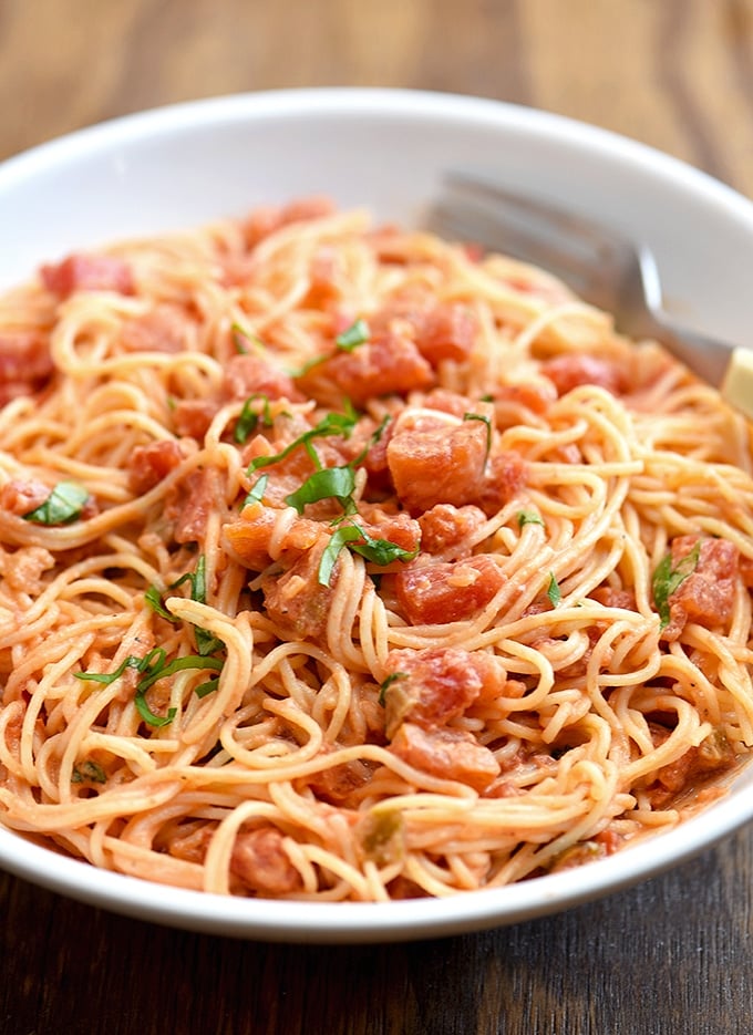 angel hair pasta tossed with chunky tomato cream sauce on white plate