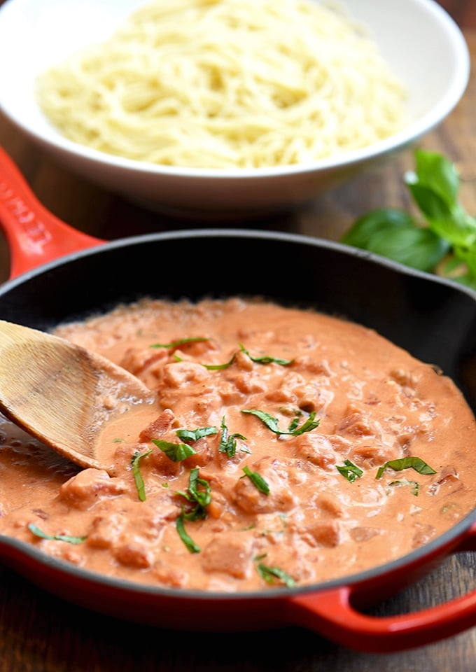 tomato cream sauce on a red skillet with a side of angel hair pasta 