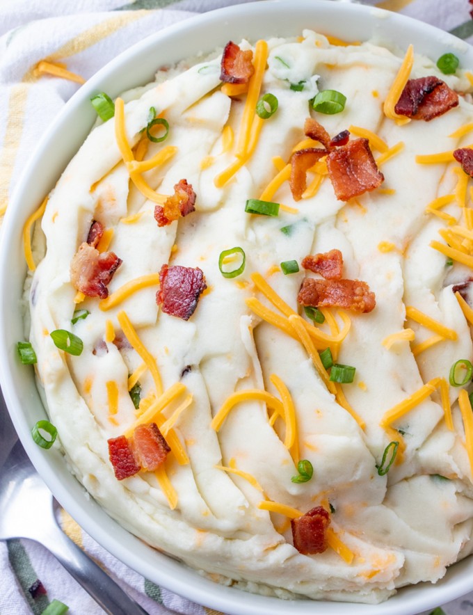 mashed potatoes with bacon, shredded cheese, and green onions in a white bowl