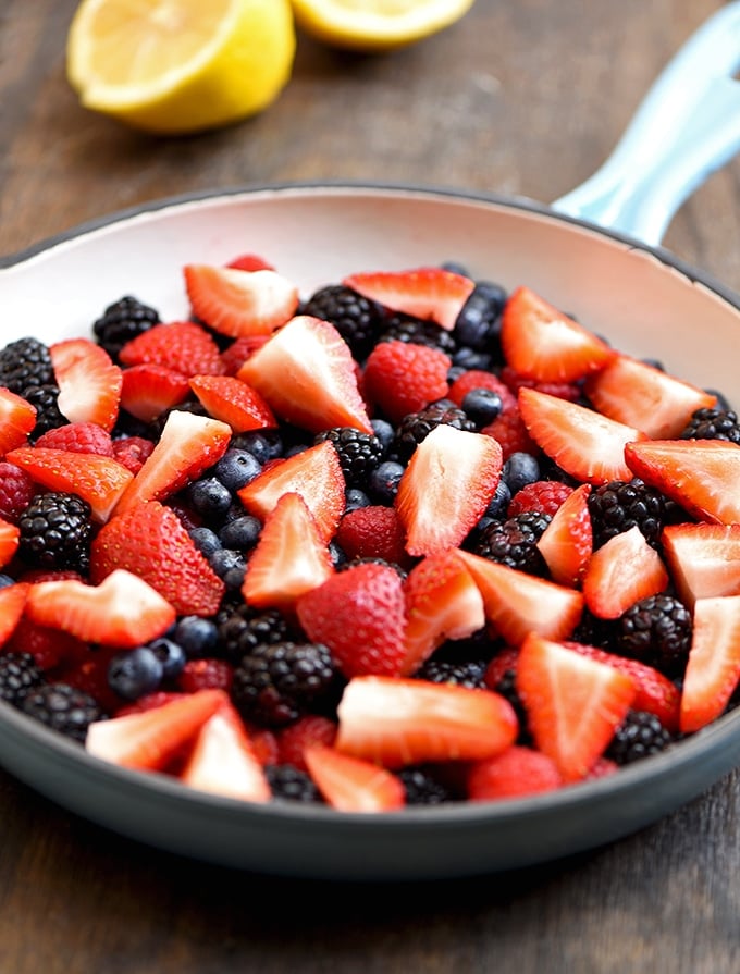 Fresh berries in a blue skillet with sliced lemon on the side to bake as fruit crisp