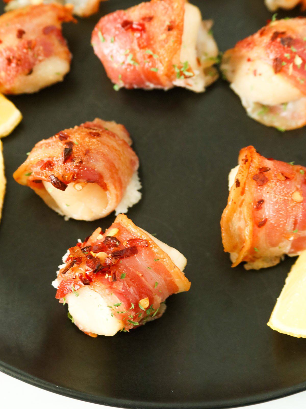 Pancetta-wrapped Scallops on a baking serving platter with as slice of lemon