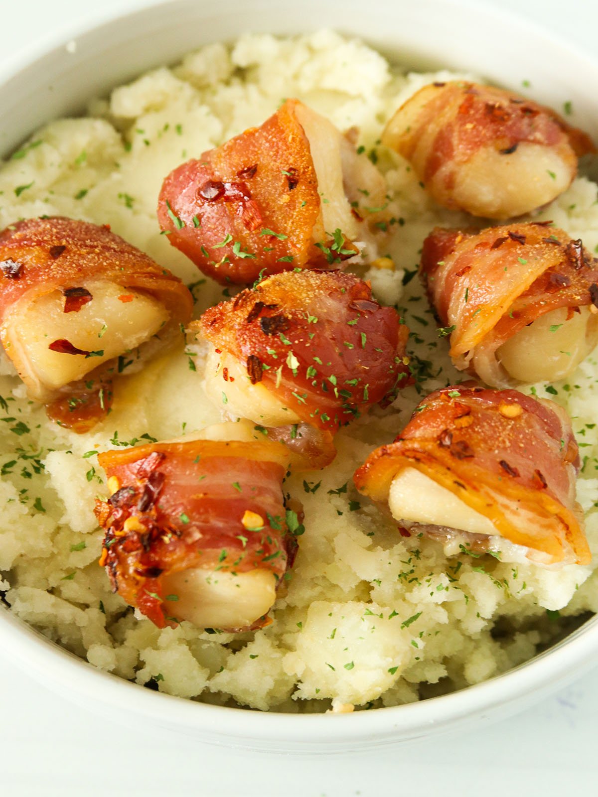 Pancetta-wrapped Scallops over mashed potatoes in a white bowl
