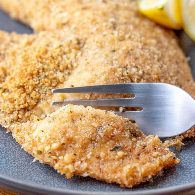 cutting baked parmesan tilapia with a fork