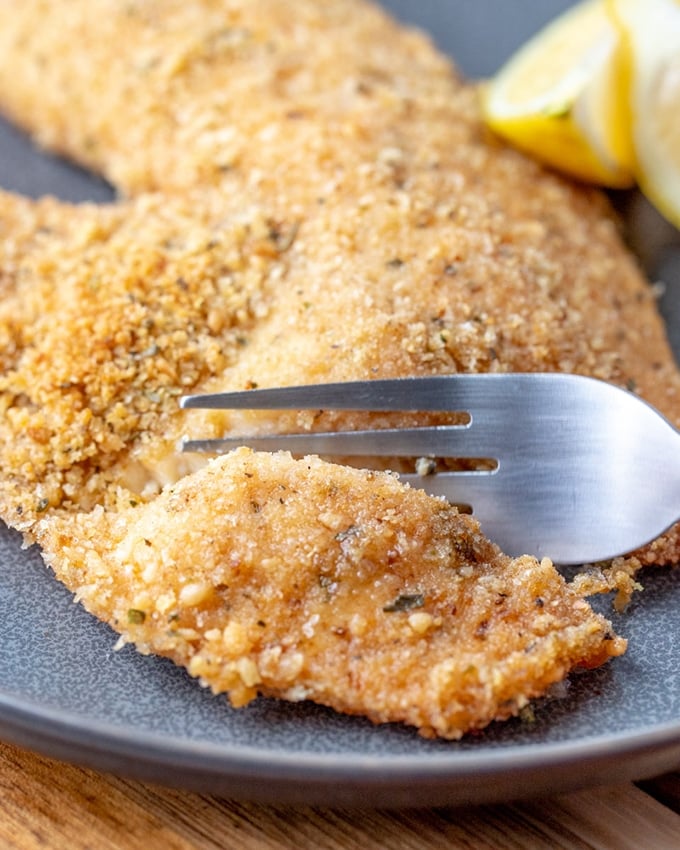 cutting baked parmesan tilapia with a fork 