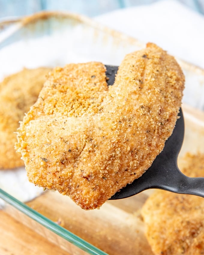 serving baked parmesan tilapia with a spatula from the baking dish