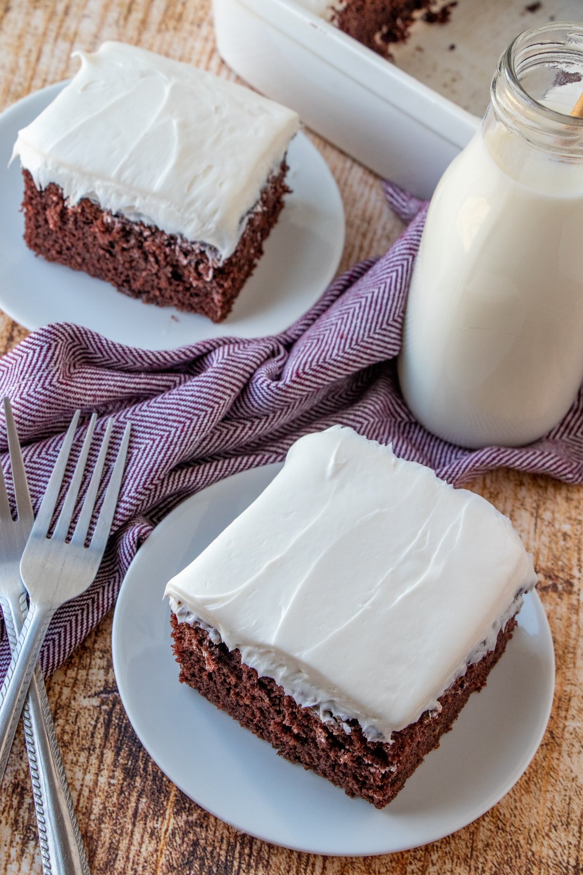 slices of Cockeyed Cake on white serving plates with jug of milk on the side