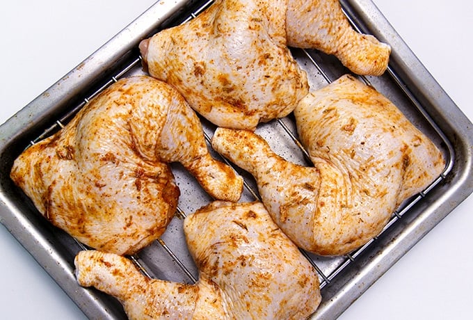 brined and seasoned chicken leg quarters on a roasting rack