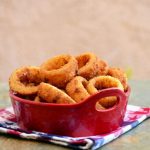 crispy onion rings in a ceramic container with a side of dipping sauce