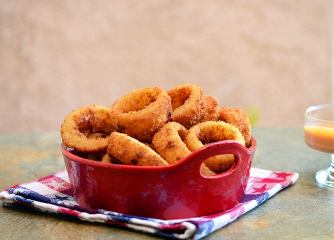 crispy onion rings in a ceramic container with a side of dipping sauce