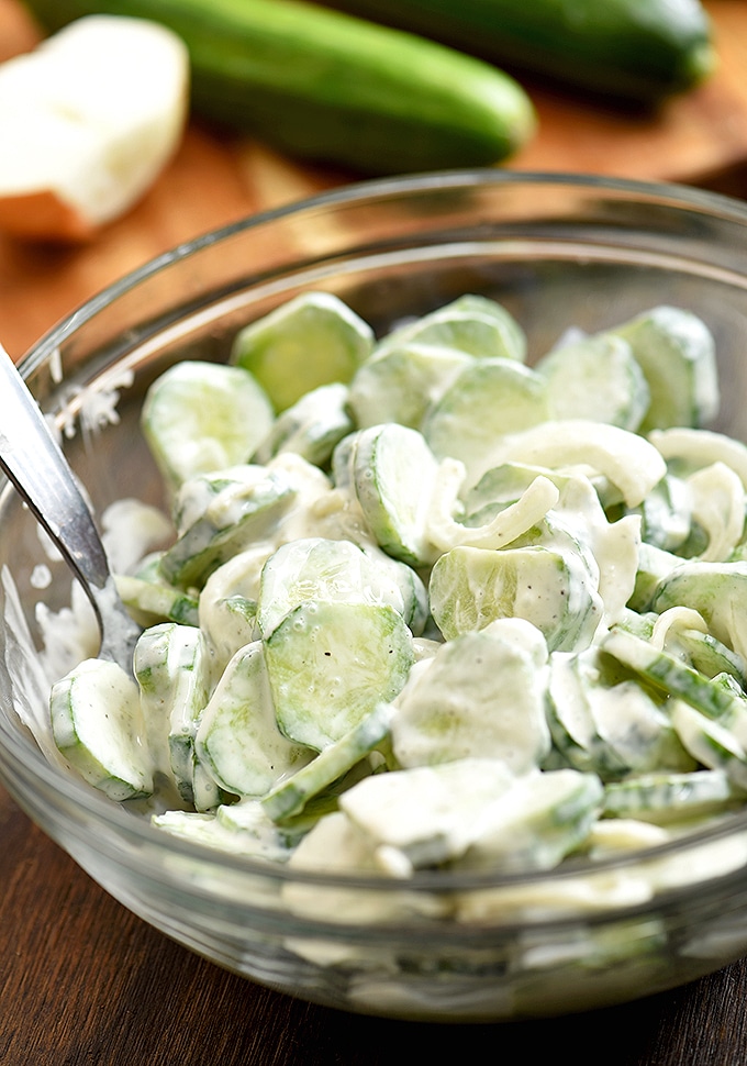 clear bowl of sliced cucumbers and sweet onions tossed in a creamy mayo dressing