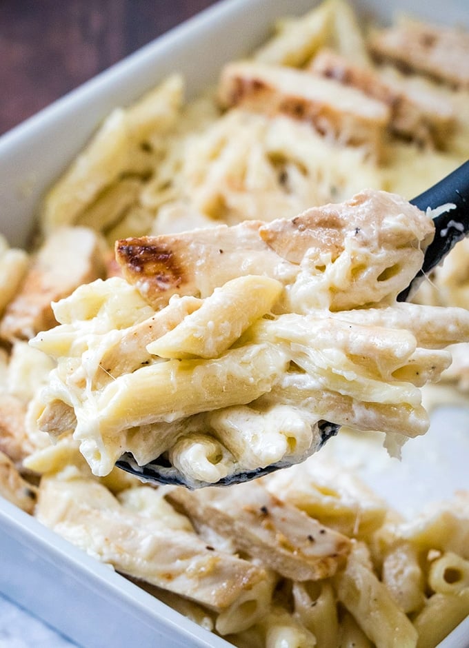 serving chicken alfredo bake from a white casserole dish with a large spoon