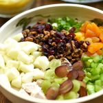 curry chicken salad with apples, grapes, dried apricots, candied walnuts, and celery in a bowl with a side of curry dressing and lettuce leaves