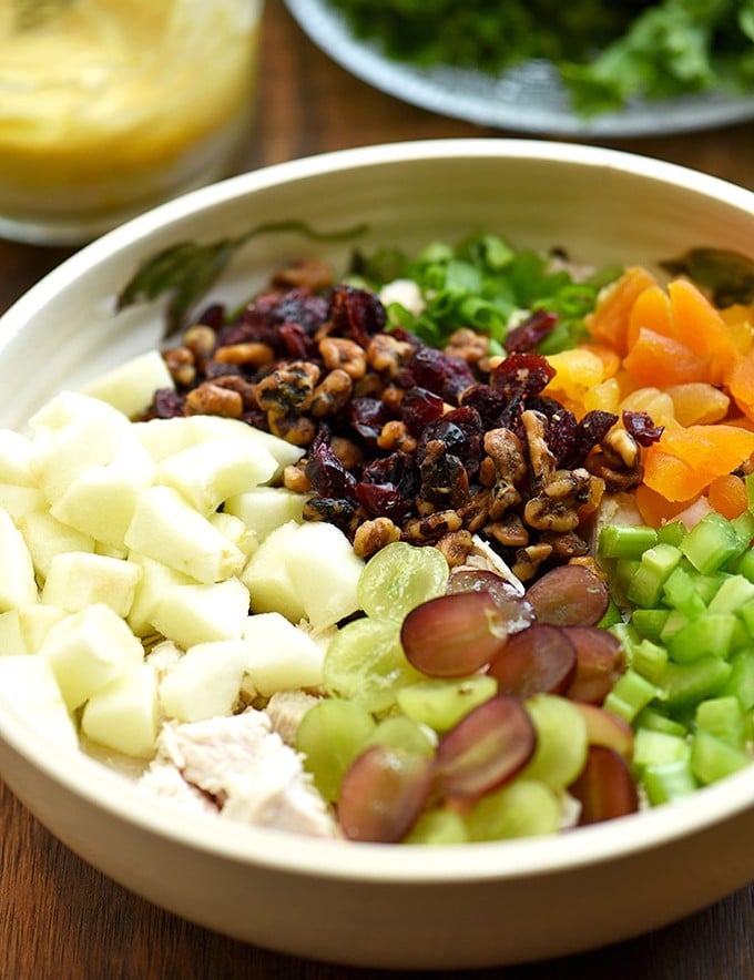 curry chicken salad with apples, grapes, dried apricots, candied walnuts, and celery in a bowl with a side of curry dressing and lettuce leaves