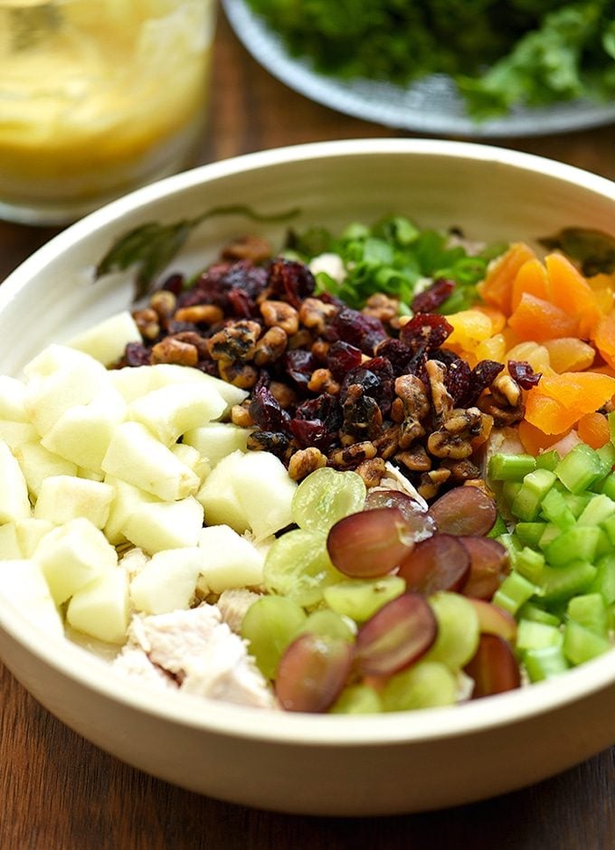 curry chicken salad with apples, grapes, dried apricots, candied walnuts, and celery in a bowl with a side of curry dressing and lettuce leaves