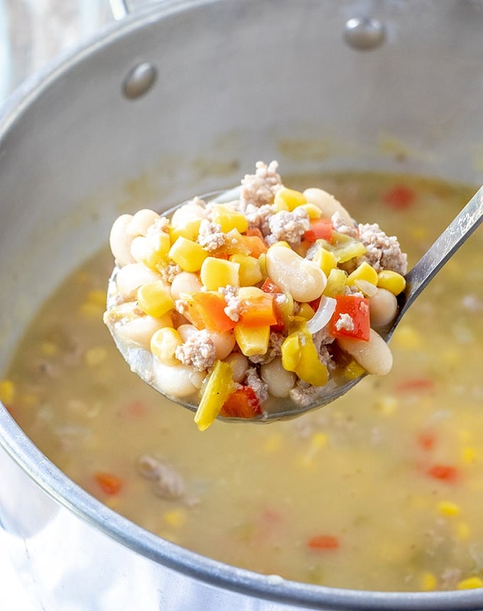 serving white turkey chili with a large ladle from pot