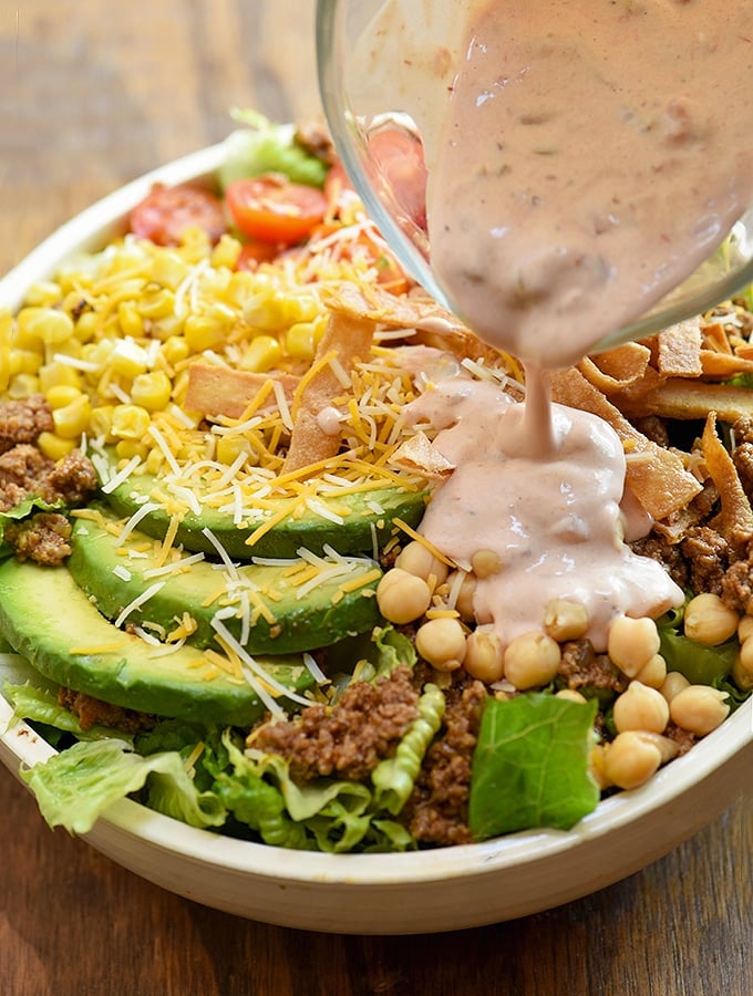 adding ranch-salsa dressing to a large bowl of taco salad