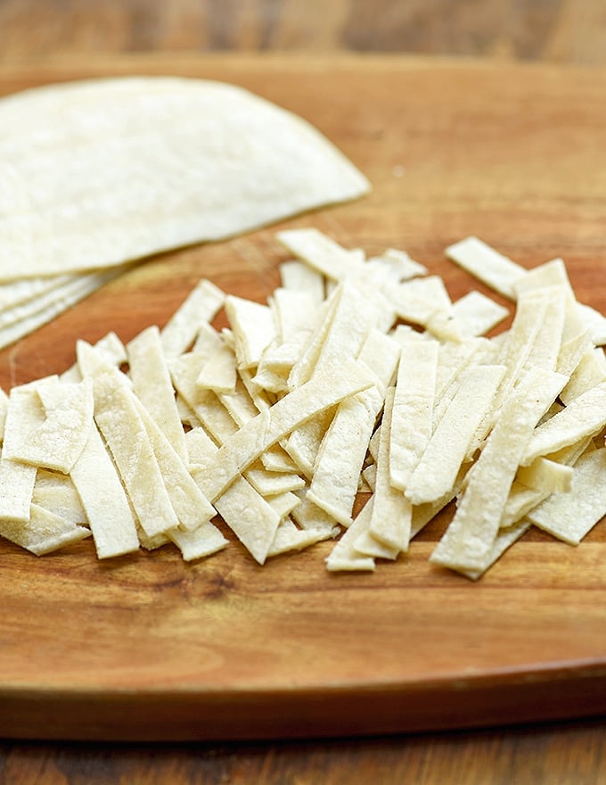 corn tortilla cut into thin strips on a wood cutting board