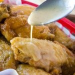 drizzling caramel sauce with a spoon on fried breaded chicken wings in a red basket