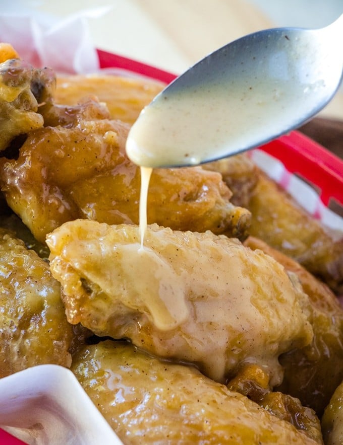 drizzling caramel sauce with a spoon on fried breaded chicken wings in a red basket