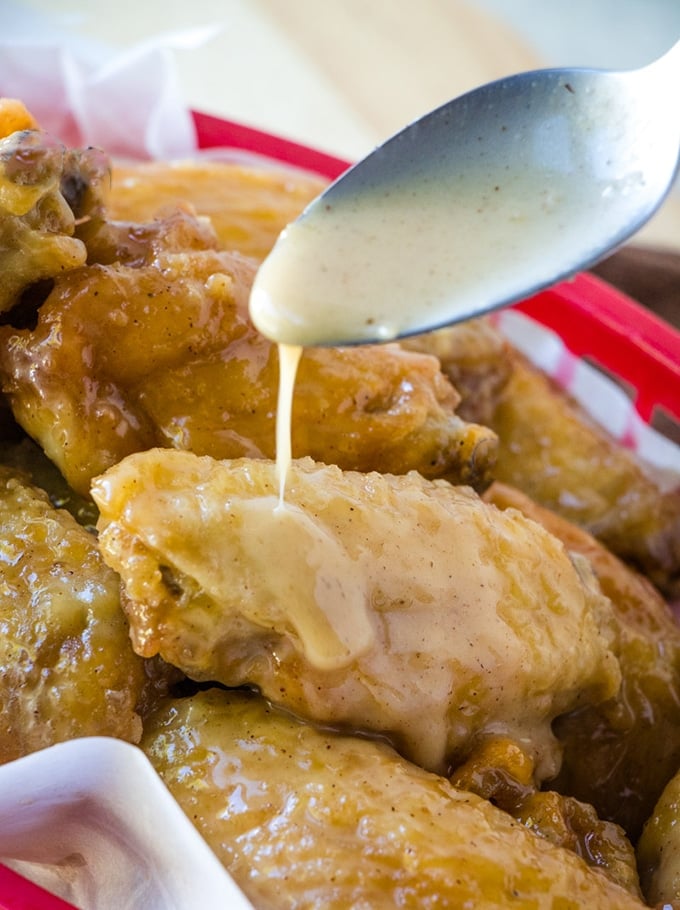 drizzling caramel sauce with a spoon on fried breaded chicken wings in a red basket