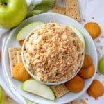Candy Crunch Dip in white serving bowl with apples, crackers, and vanilla wafers in the background.