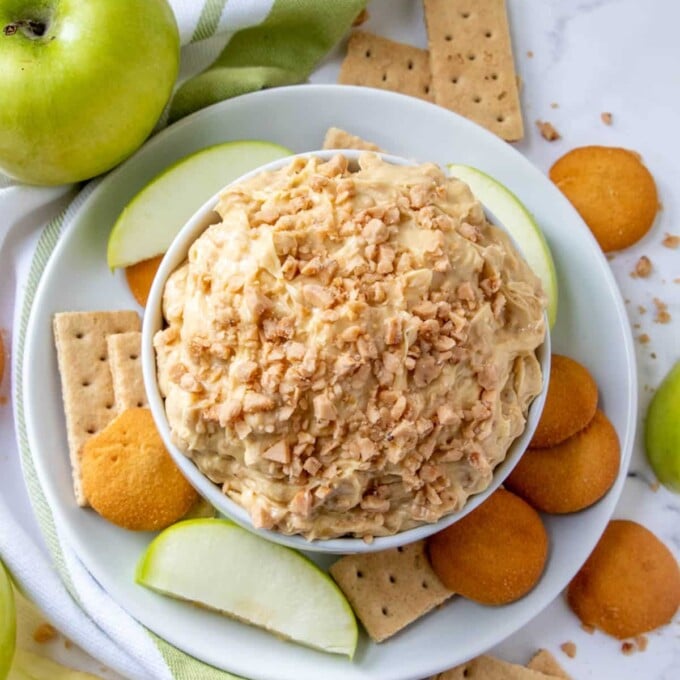 Candy Crunch Dip in white serving bowl with apples, crackers, and vanilla wafers in the background.