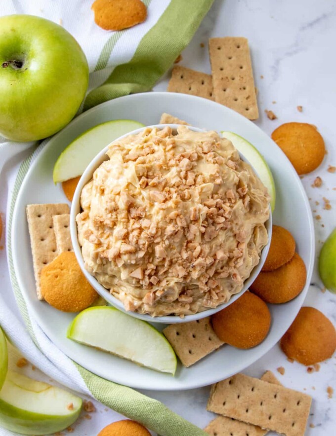 Candy Crunch Dip in white serving bowl with apples, crackers, and vanilla wafers in the background.