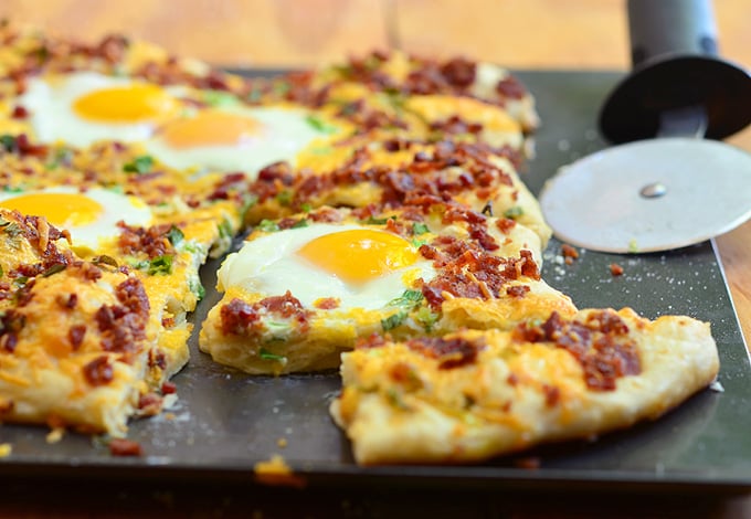 Cheesy Breakfast Pizza topped with crumbled bacon, sharp cheddar cheese, and sunny-side up eggs. Hearty and delicious, it's the best way to start your day!