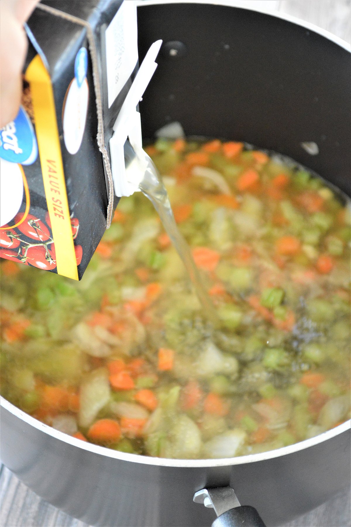 adding chicken broth to sauteed onions, carrots, and celery in a pot