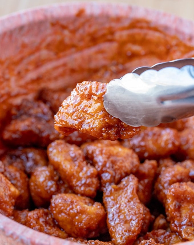 serving cajun buffalo boneless wings with tongs from a bowl