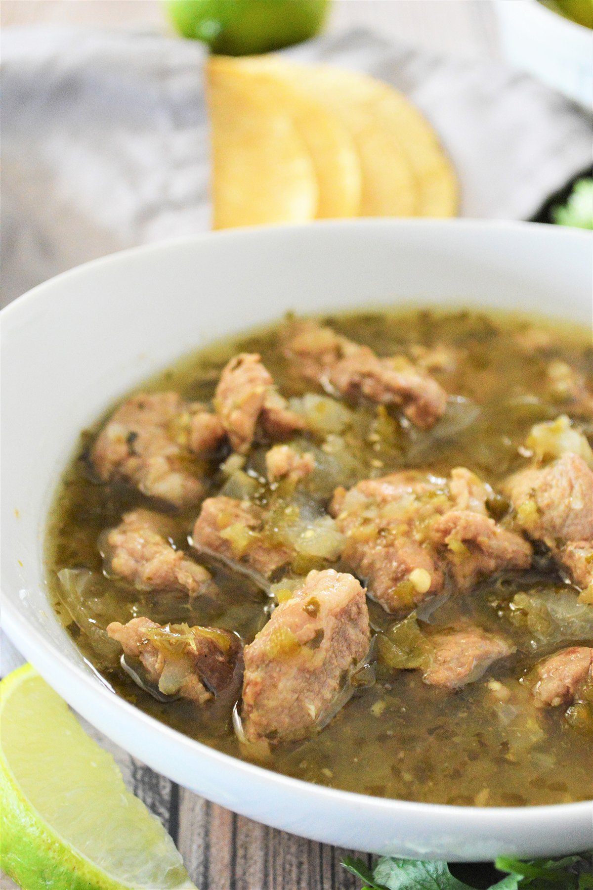 chili verde with pork in a white bowl with corn tortillas on the side