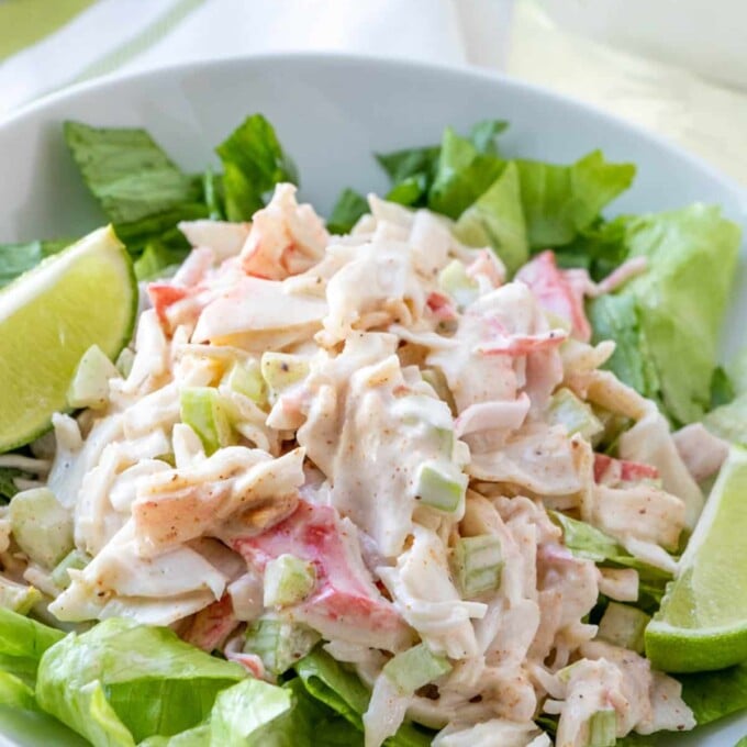 imitation crab salad on a bed of lettuce with slices of lime on the side in a white plate.