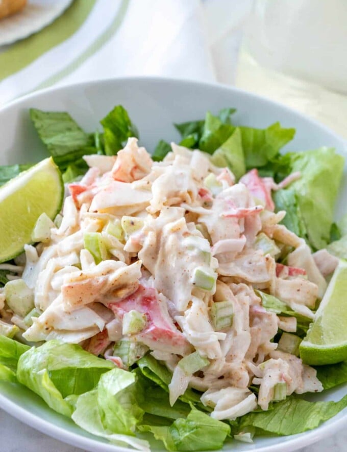 imitation crab salad on a bed of lettuce with slices of lime on the side in a white plate.