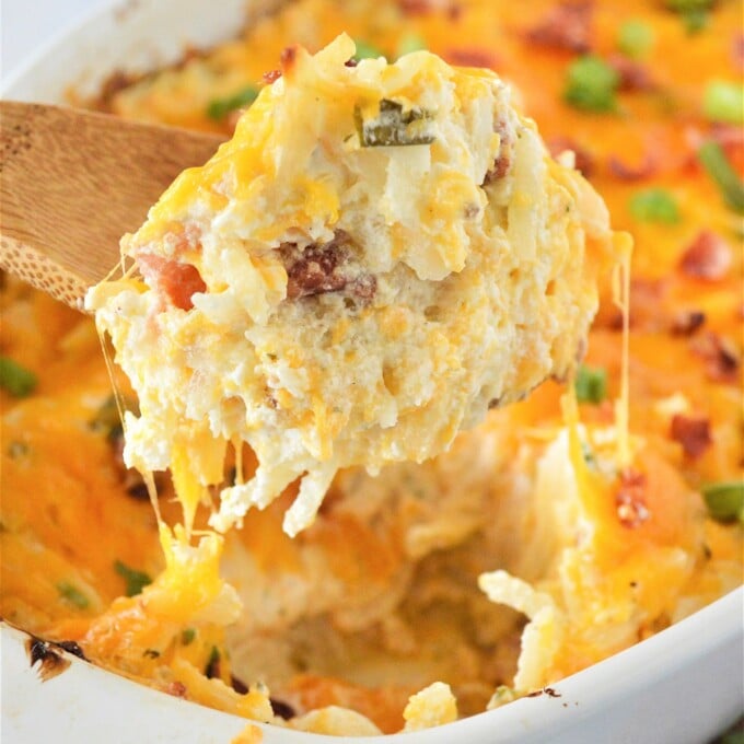 serving crack potatoes from a white dish with a wooden spoon.