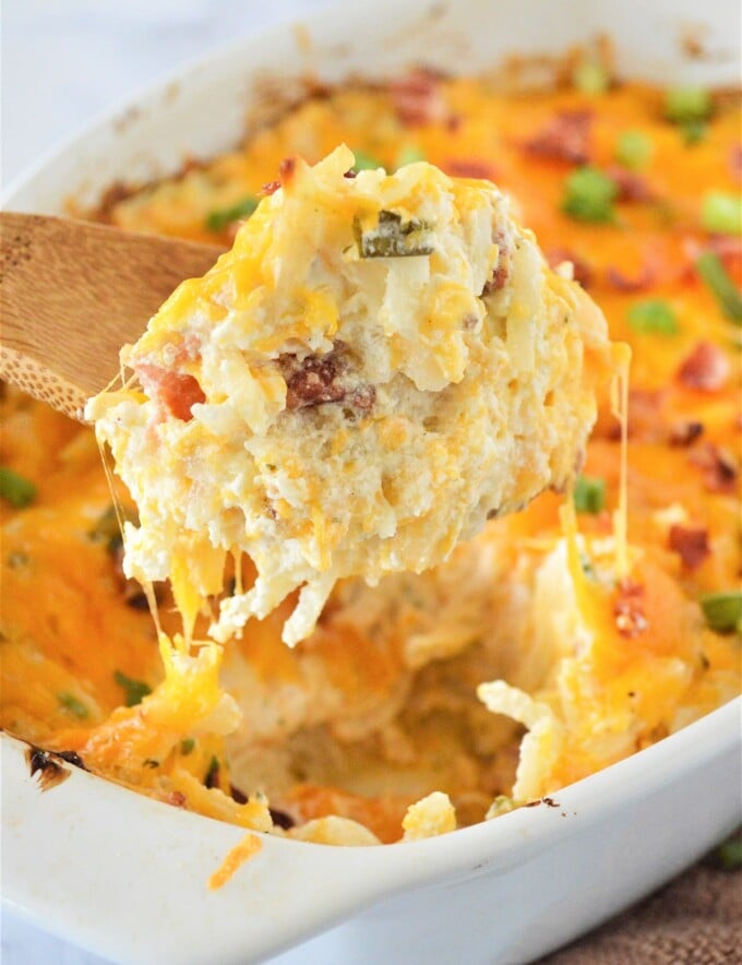 serving crack potatoes from a white dish with a wooden spoon.