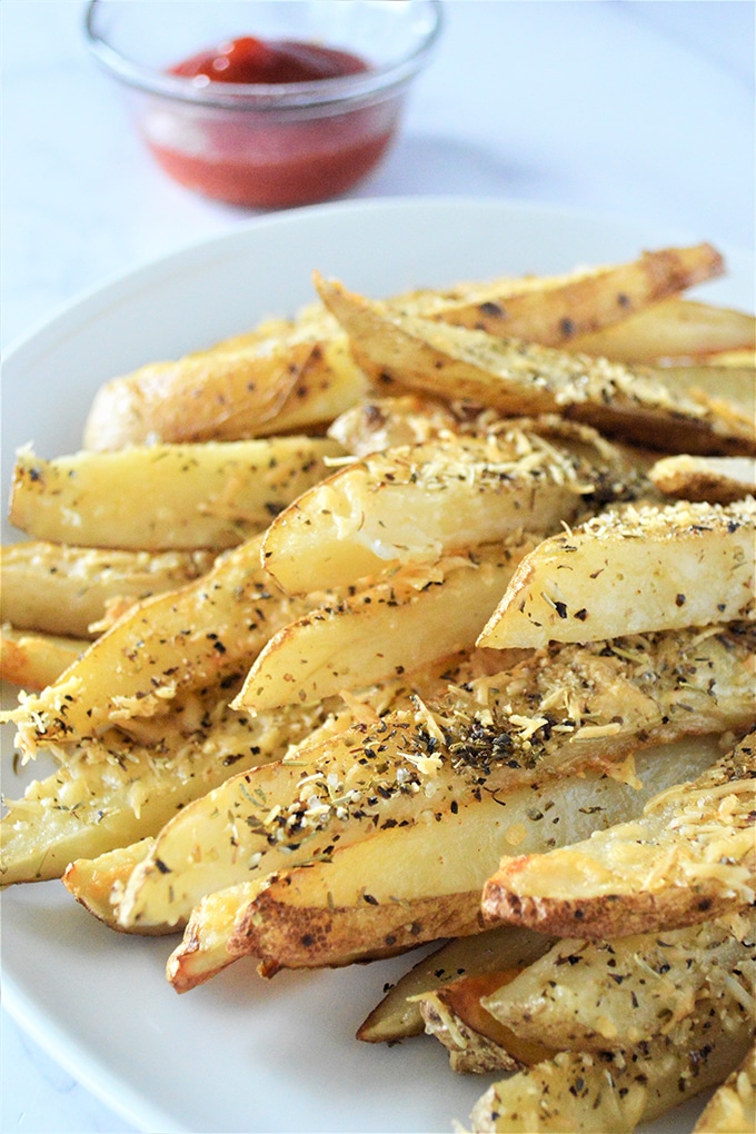 Baked Parmesan Potato Wedges are golden, crisp and loaded with delicious Parmesan and garlic flavors yet baked for a less-guilt snacking! on a plate with a side or ketchup