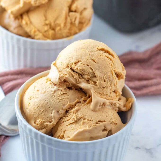 scoops of dulce de leche ice cream in white bowls with a metal loaf pan of ice cream in the background.