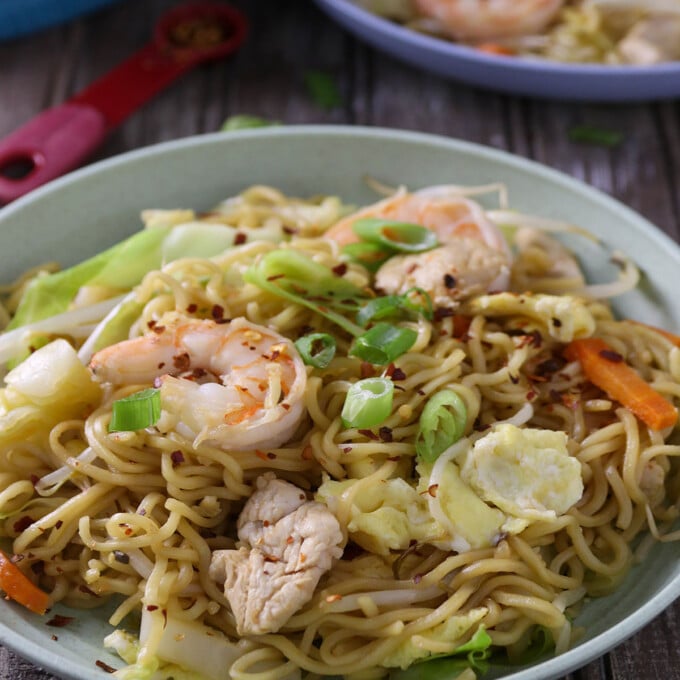 Spicy dragon noodles made of ramen, shrimp, chicken, and vegetables in a white serving bowl