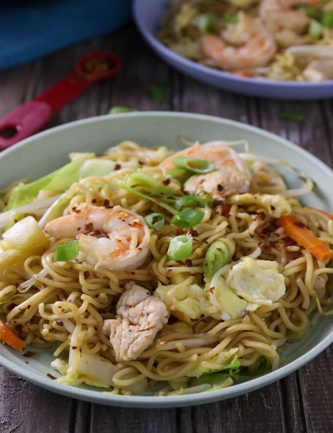 Spicy dragon noodles made of ramen, shrimp, chicken, and vegetables in a white serving bowl