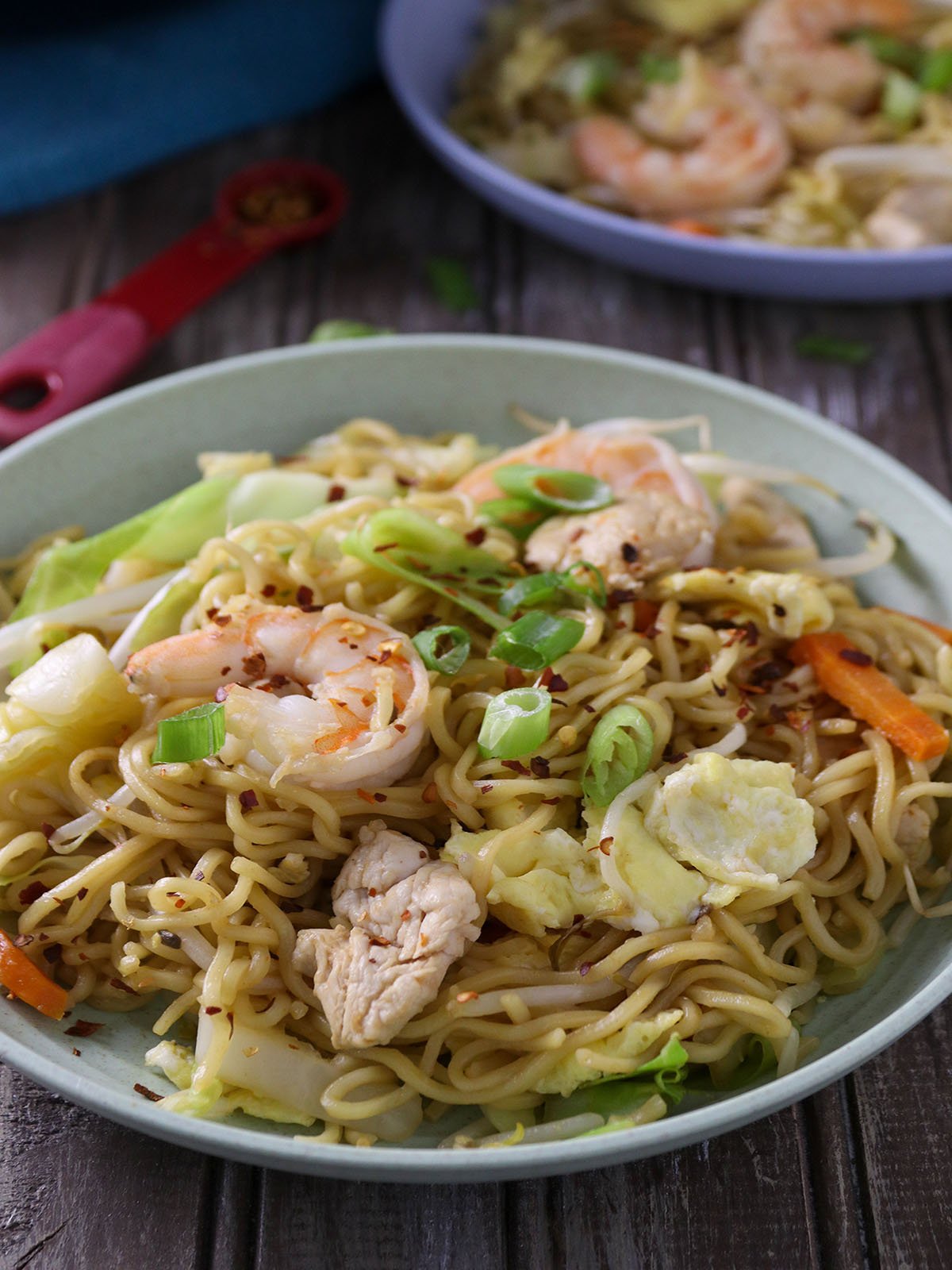 Spicy dragon noodles made of ramen, shrimp, chicken, and vegetables in a white serving bowl