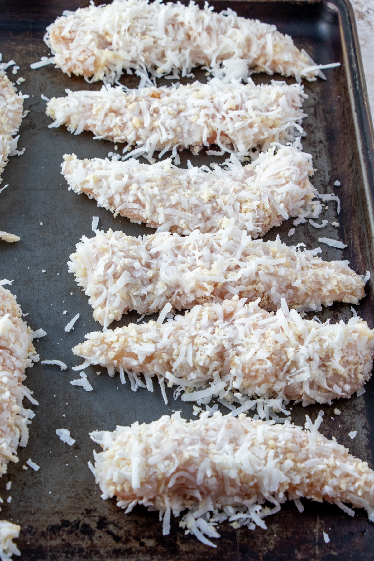 coconut breaded chicken tenders on a baking sheet