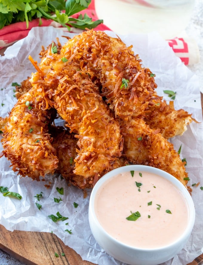 Coconut Chicken Tenders on a parchment paper with a small bowl of dipping sauce on the side