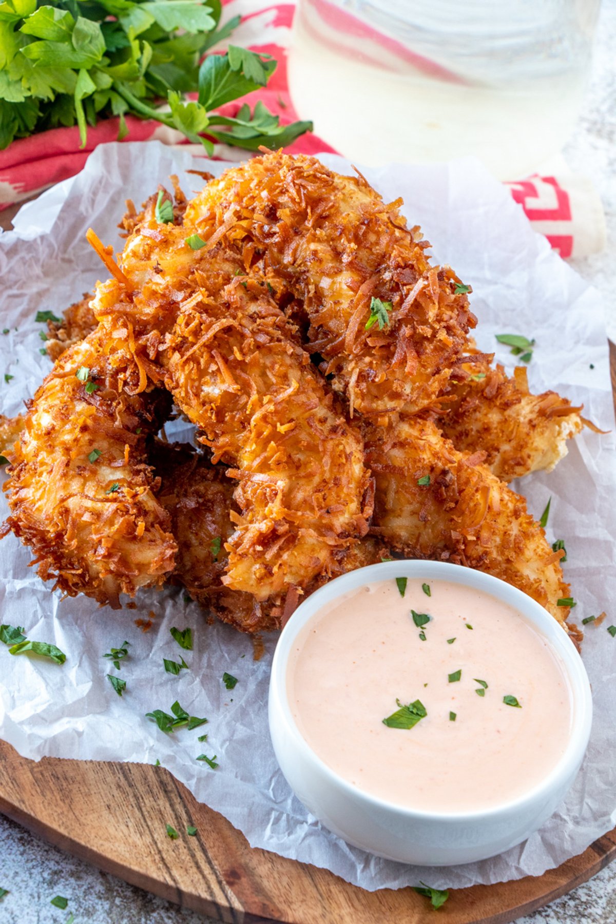 Coconut Chicken Tenders on a parchment paper with a small bowl of dipping sauce on the side